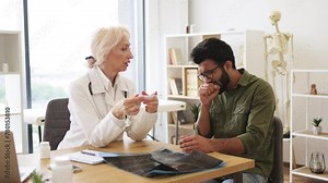 Female general practitioner in white uniform communicating with young coughing patient in new clinic. Doctor discussing health issues and measures temperature for treatment of disease.