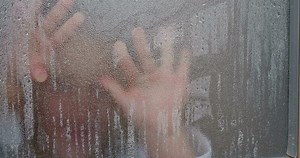 Kid wiping steamy window to look outside