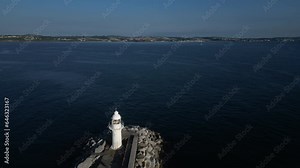 Brixham, Torbay, South Devon, England: DRONE VIEWS: Reverse shot over Brixham Harbour Lighthouse and flies parallel to the Outer Harbour Wall. Brixham is a fishing port and a popular UK holiday resort