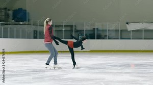 Panning shot of figure skating training where coach helping little skater to slide on ice inside ice rink