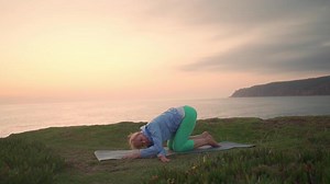 Senior woman practicing yoga exercise on the beach.