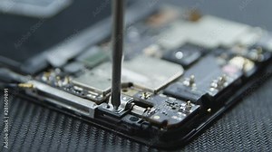 Close-up shot showing the process of cell phone repairing. Hands of repairer getting out the screws with a screwdriver. The internal components of a smartphone. Disassembled cell phone.