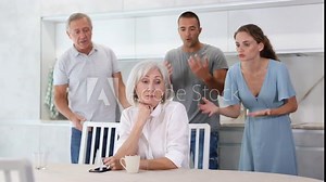 Woman sits at table in kitchen and pretends not to understand her family. High quality 4k footage