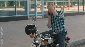 Young man motorcyclist talking on the phone while sitting on custom motorcycle