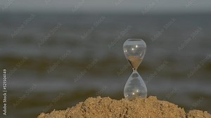 Waste of time concept. Glass hourglass on sandy beach on sea background. Time management.