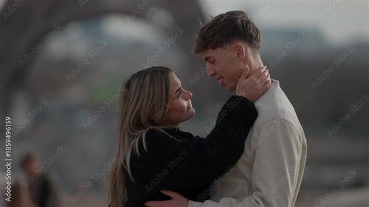 A romantic couple in Paris France near the Eiffel Tower The woman gently touches the man's Shallow depth of field creates a soft intimate atmosphere The scene captures a love story in a popular travel