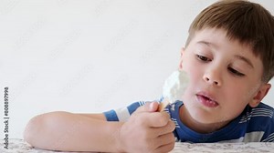 Handsome boy eating popsicle on a stick. He bites off the ice cream with pleasure. Close-up. Child eat in the kitchen or at the dining room table. Tasty dessert. Slow motion. High quality 4k footage