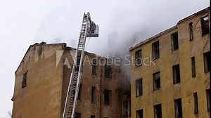 Silhouette of firefighter on turntable ladder fighting fire on burning abandoned building