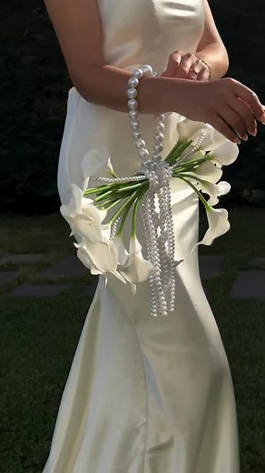 Not just a bouquet — but an extension of her bridal silhouette. Sculptural calla lilies wrapped in strands of pearls, merging floral design with fashion. A quiet kind of statement that lingers. @kalibridal #thebrideway #thebridewyweddings #bridalbouquet | The Bride Way