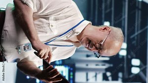 Vertical video Precise IT professional navigating network of server rows in industrial hub. Computer operator with laptop ensuring proper operations, doing optimizations and maintenance in data center