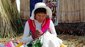 Young Latin American peruvian woman wearing traditional clothes weaving colorful cloth textile at floating islands of Uros, Lake Titicaca, Puno. Aymara indigenous people. Handmade traditional.