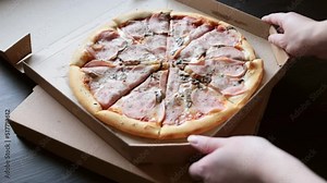 Delivery of pizza in a box. Girl opens a box with delicious juicy pizza