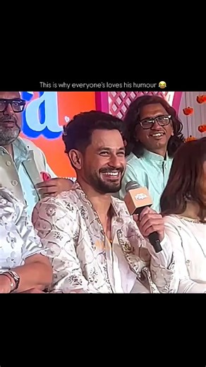 Kunal Kemmu smiling and speaking into a microphone, surrounded by other cast members,