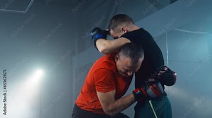Two fighters show their strength, agility and determination. Athletic fighter in boxing gloves exercises with male trainer. Fighters training at smoky background. 4K, UHD
