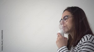 A young woman breathes through an inhaler mask closeup. A girl in glasses with an oxygen mask is being treated for a respiratory infection.
