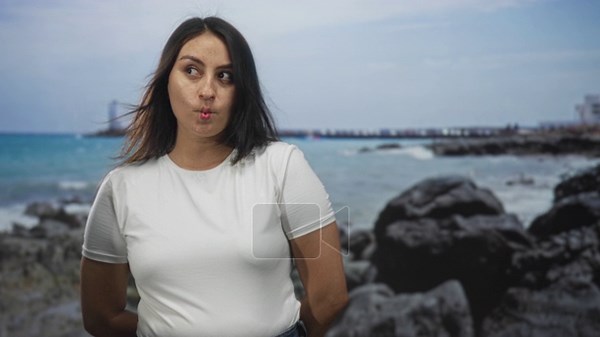 Woman with puckered lips and windblown hair poses with hands behind back on rocky beach by the sea; playfulness Stock Video Footage - Alamy