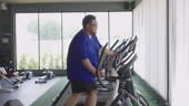 Slow motion Side view of overweight young man jogging on eliptical...