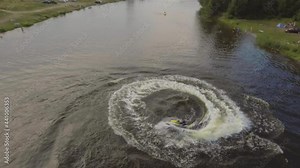 Girl riding a jet ski on the river in a summer sunny day.Aerial view:Teen girl having fun jumping a wave riding yellow and white jet ski in the river.Rider on jet sk rides in a circle on the river