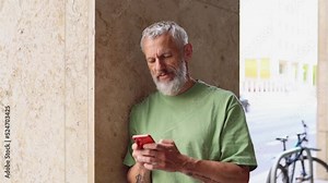 Mature gray-haired older middle aged bearded man using moble cell phone outdoors. Happy old senior adult male user holding cellphone texting typing message on smartphone digital technology.