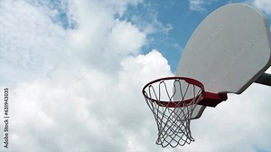 pan left from outdoor basketball net with white backboard and mesh with silver post protruding from its back, ending on clouds in background