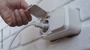 Hand inserting electrical plug into and plug out socket and on white wall close up, depicting energy use and power connectivity. Daily life, technology and household activities.