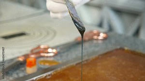 A close-up of a pastry chef pours dye on liquid caramel in a pastry shop to create a bright color. The production process of lollipops and caramel candies.