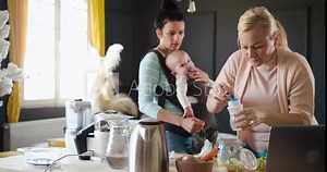 Grandmother preparing baby formula in the baby bottle, while the daughter calms the crying baby.