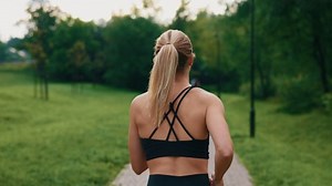 Back view of the female runner is running in the park wearing sport clothes. Sporty woman jogging exercising outdoors at sunrise. Close up. People and sport concept