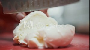 Cutting mozzarella ball on thin slices. Close up view of slicing large mozzarella ball into thin slices with a knife