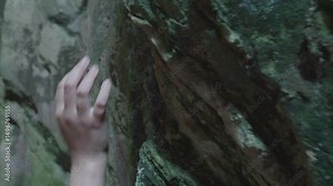 Female hiker exploring rocky cave interior, touching weathered stone walls, feeling geological details while immersing in underground wilderness landscape