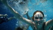 Medium shot of young people having fun under water in pool. They are...