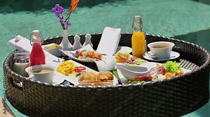 Luxurious floating breakfast tray in swimming pool at tropical resort. Gourmet holiday experience with fresh fruits, pastries, juices, and hot beverages. Exotic vacation dining and leisure.