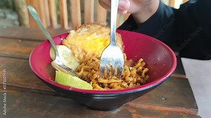 Close up of a fork wrapping noodles around the fork in a rotating manner. Brown noodles are served in an Asian restaurant on a plate.
