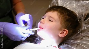 A happy young boy smiles while getting his teeth cleaned at the dentist. He does not want to let go of the sucking rinser tube and keeps his mouth open while waiting for hygienist to return.