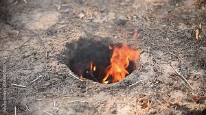 A Dakota fire pit burning in a small hole in the ground, creating an efficient and smokeless flame. Perfect for wilderness survival, bushcraft, and outdoor adventure themes