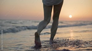 Beautiful female legs walking on the sea waves at sunset