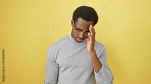 Furious young african american man yelling in a frenzy, glasses gleaming and arms shouting defiance - an epitome of crazy anger over yellow isolated backdrop.