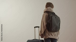 Young adult woman with a backpack, a suitcase and paper documents on a white background. Back view. Foreign student. Refugee or immigrant
