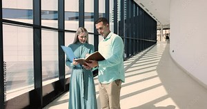 Two Caucasian workmates having discussion over joint project standing in office hallway. Millennial male boss explain task to colleague or secretary learn agreement details, consider agenda. Workflow