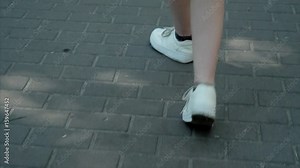Young beautiful female feet in sneakers walking on the tile shape rhombus summer on a hot day