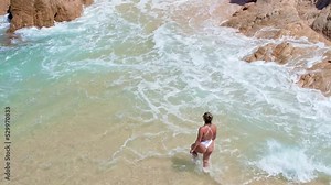shot of a beautiful woman in a white bikini walking along the sandy and brown rocky shore. revel, relax, reset and recharge in Cabo San Lucas, Baja California. 4K videos.