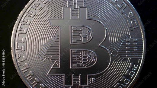 Macro close-up of a silver physical Bitcoin coin with intricate circuitry patterns and the iconic B symbol against a dark, minimal background