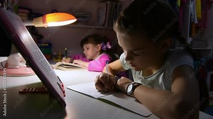 The sisters do homework late at night, sitting at the table, one of them wants to sleep and yawns