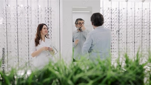 Optometrist assisting customer trying on new eyeglasses in an optical shop, focusing on clear vision and eye care