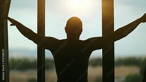 Man opens the curtains in the morning and looks out the window. Young man opens big window curtains and lets the sun light in the room