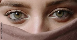 Face of muslim girl wearing traditional hijab head scarf and makep. Her eyes with brown and green irises sensually looking at camera - beauty concept extreme close up shot 4k footage