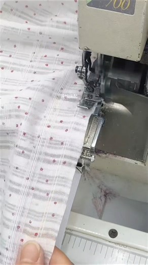 sewing machine actively stitching a piece of light-colored fabric with a subtle red pattern.