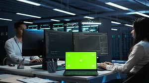 Engineer in high tech data center managing and maintaining databases using mockup devices, ensuring data integrity. Indian employees updating server room supercomputers with chroma key laptop