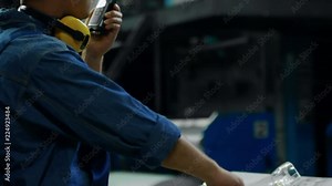 Tilt down shot of male factory worker in protective equipment using two way radio when operating printing press