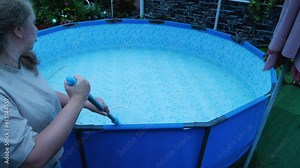 Caucasian woman cleans the bottom of the pool with an underwater vacuum cleaner-brush. Cleaning and filling the pool with water at the beginning of the summer season
